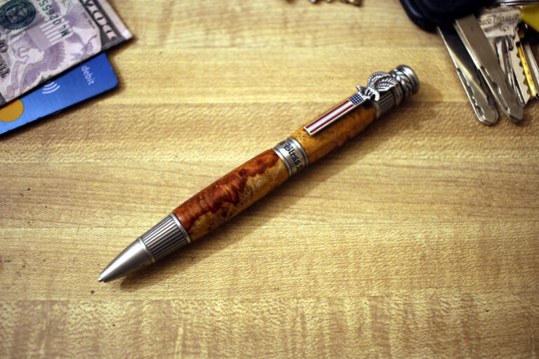 This is a ballpoint pen known as the American Patriot. It features a body made of antique pewter and is accented with amboyna burl wood. The combination of materials gives the pen a distinctive and elegant appearance.